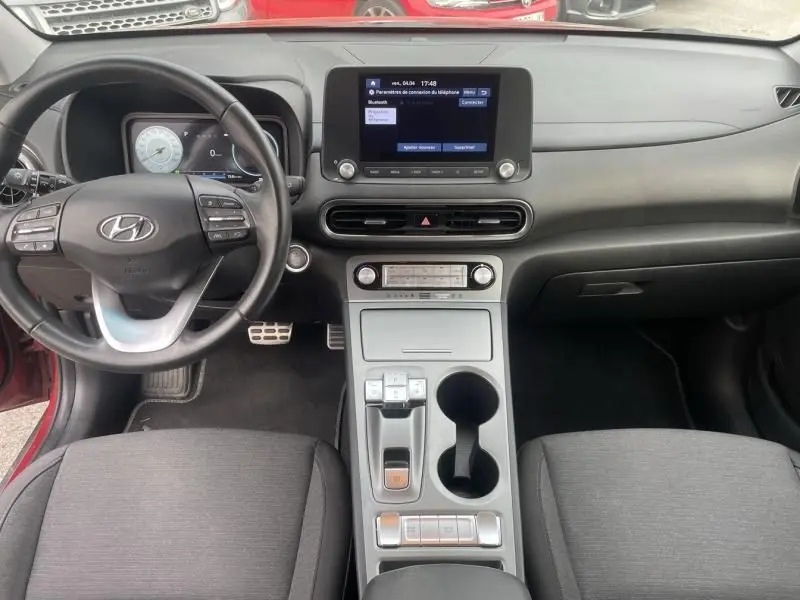Vue intérieure du tableau de bord et console centrale du Hyundai Kona électrique rouge métal 2021 avec écran tactile et volant multifonction.