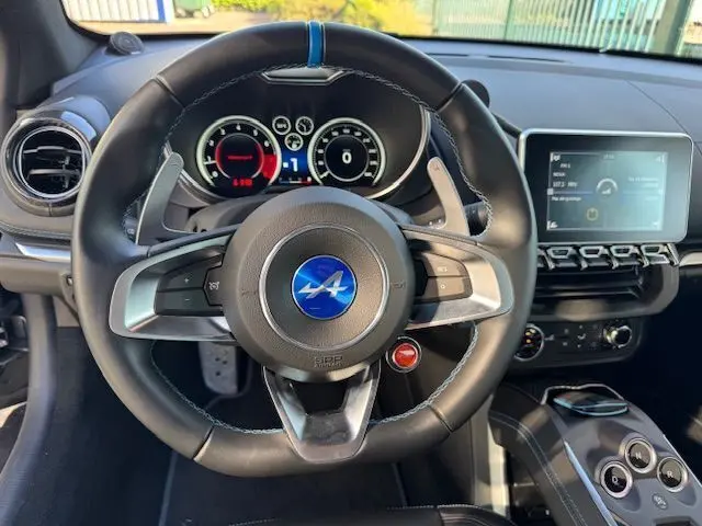 Vue centrée sur le volant cuir noir avec logo Alpine bleu, tableau de bord numérique et console centrale carbone brillant de l'Alpine A110.