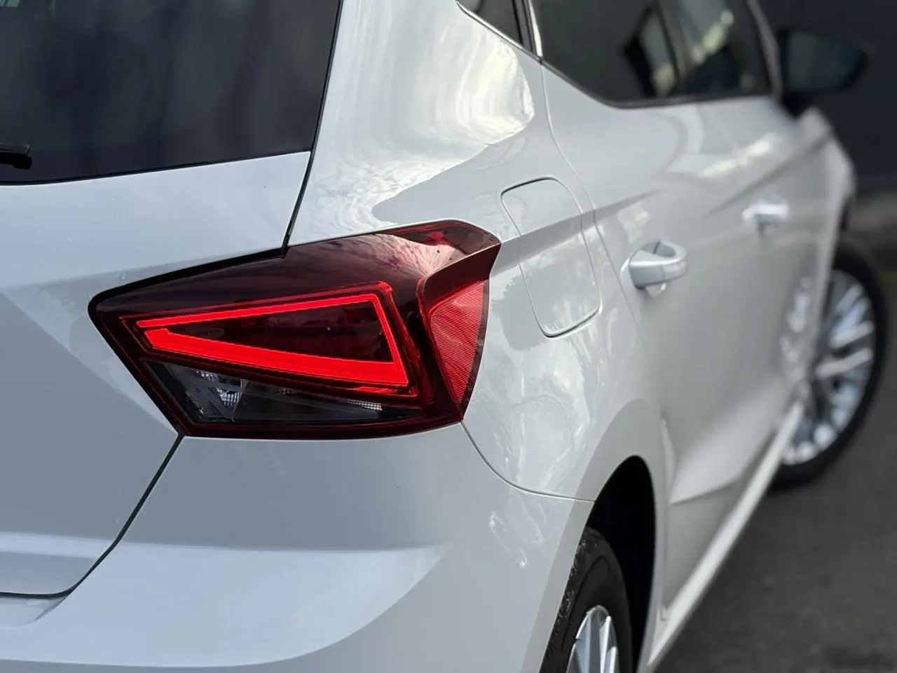 Gros plan sur le feu arrière gauche rouge d'une SEAT Ibiza blanche vue de trois quarts arrière côté gauche.
