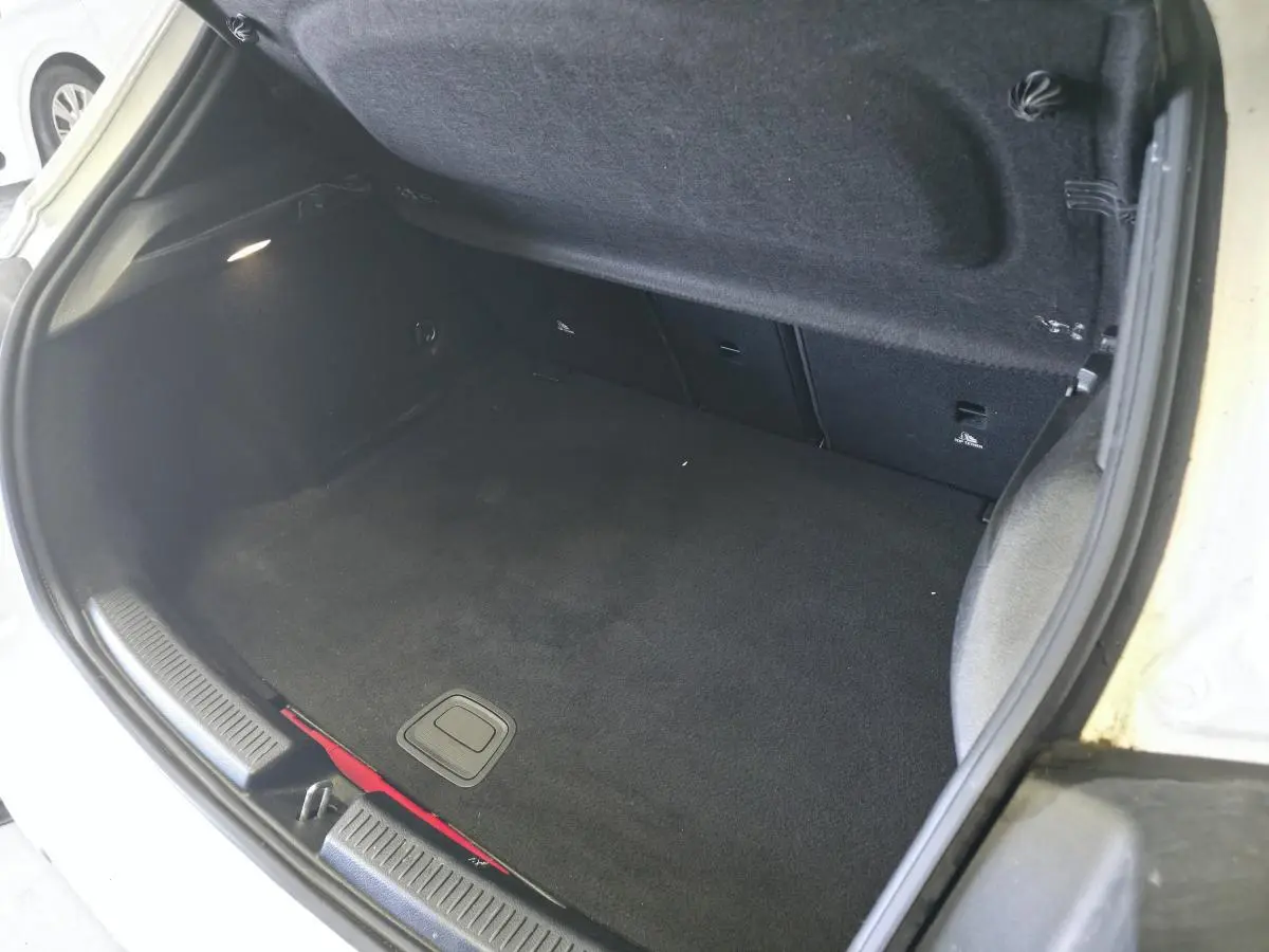Coffre ouvert vu de l'arrière d'une Mercedes Classe A 160 Style Line blanche, intérieur noir et tapis propre.