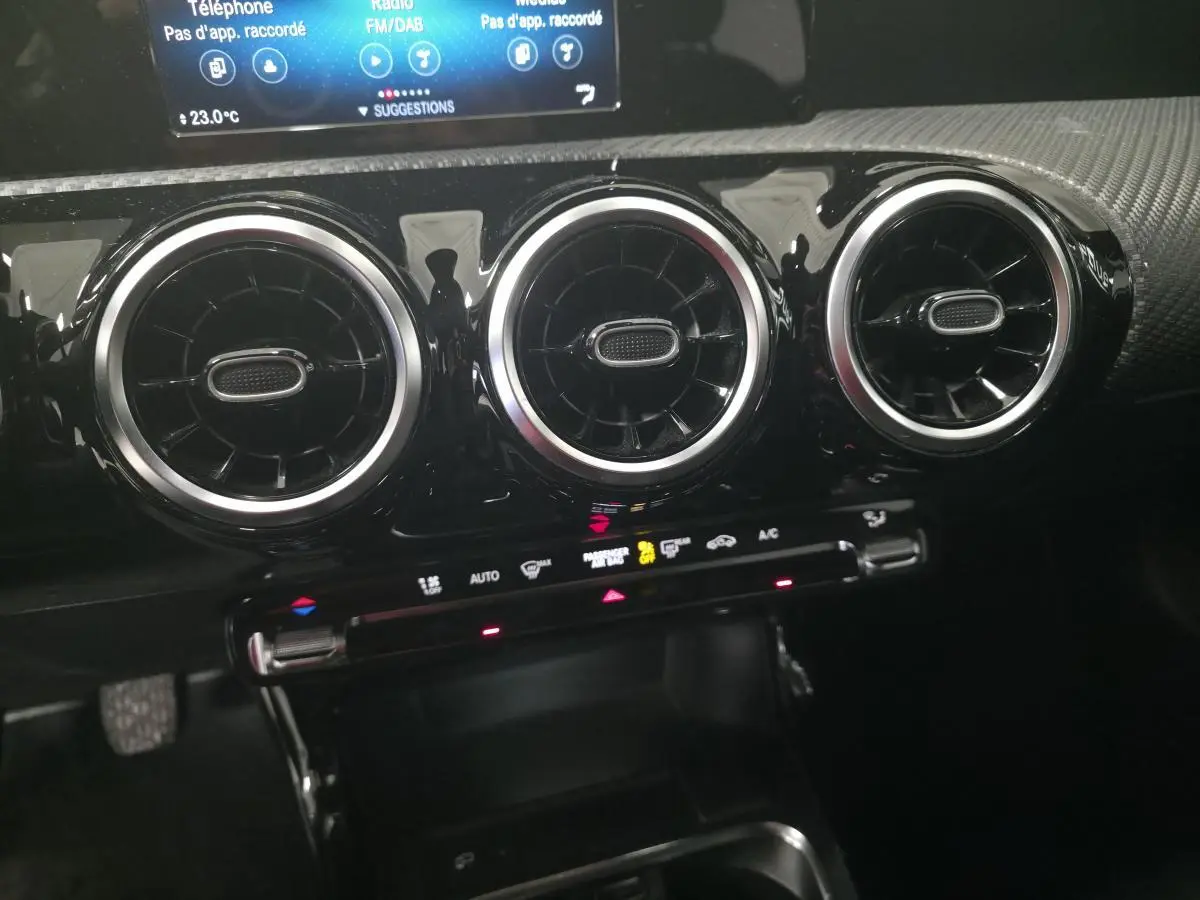 Gros plan sur les aérateurs ronds chromés et la console centrale noire du tableau de bord d'une Mercedes Classe A blanche.