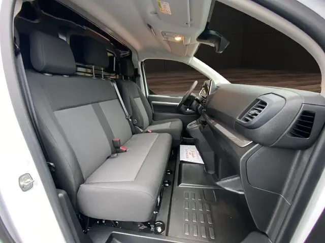Vue intérieure côté conducteur du Citroën Jumpy blanc, montrant les sièges gris et le tableau de bord moderne.