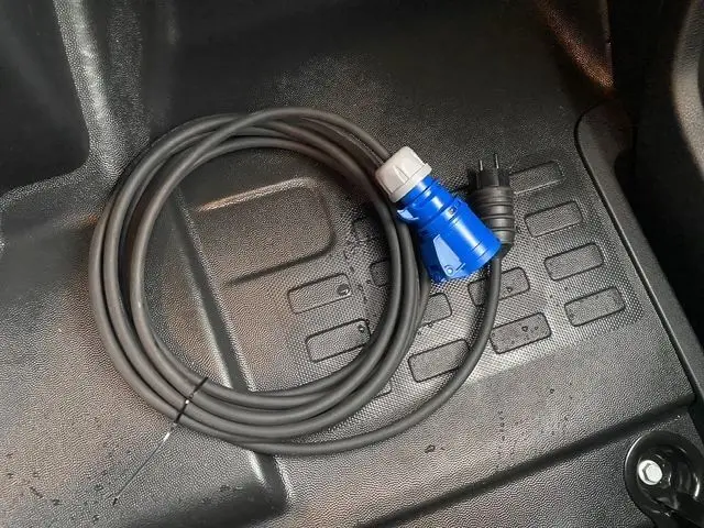 Câble électrique noir avec prise bleue et prise noire posé sur le plancher intérieur du Citroën Jumpy XL blanc.