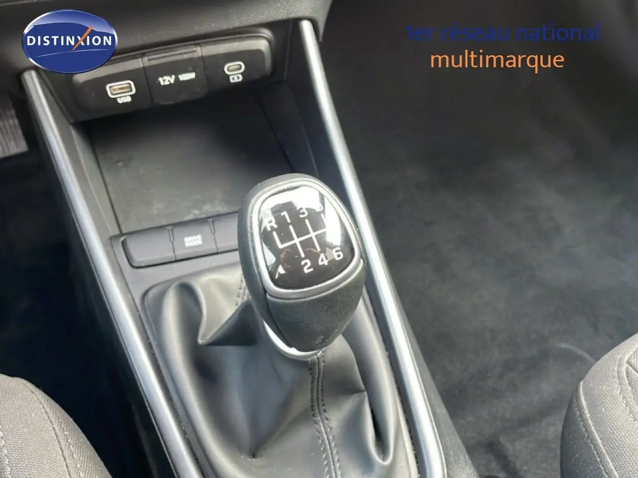 Gros plan sur le levier de vitesses manuel noir de la Hyundai i20 2025, avec console centrale et prises USB visibles.