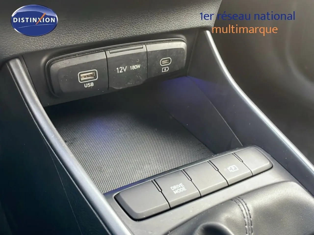 Gros plan sur la console centrale de la Hyundai i20 2025, montrant les ports USB, prise 12V et boutons de mode de conduite.