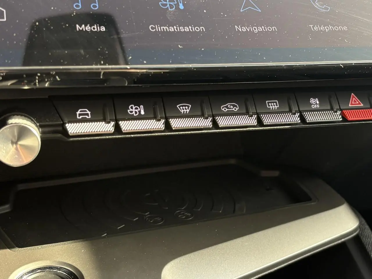 Gros plan sur la console centrale de la Peugeot 308 Hybrid 2025, montrant les boutons de commande et le chargeur à induction.