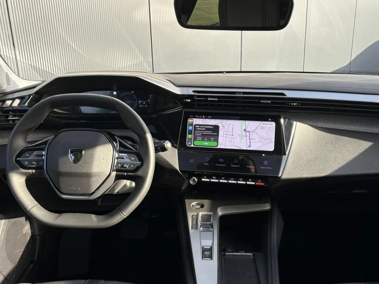 Vue intérieure frontale du poste de conduite de la Peugeot 308 Hybrid 2025 avec écran tactile et volant cuir noir.