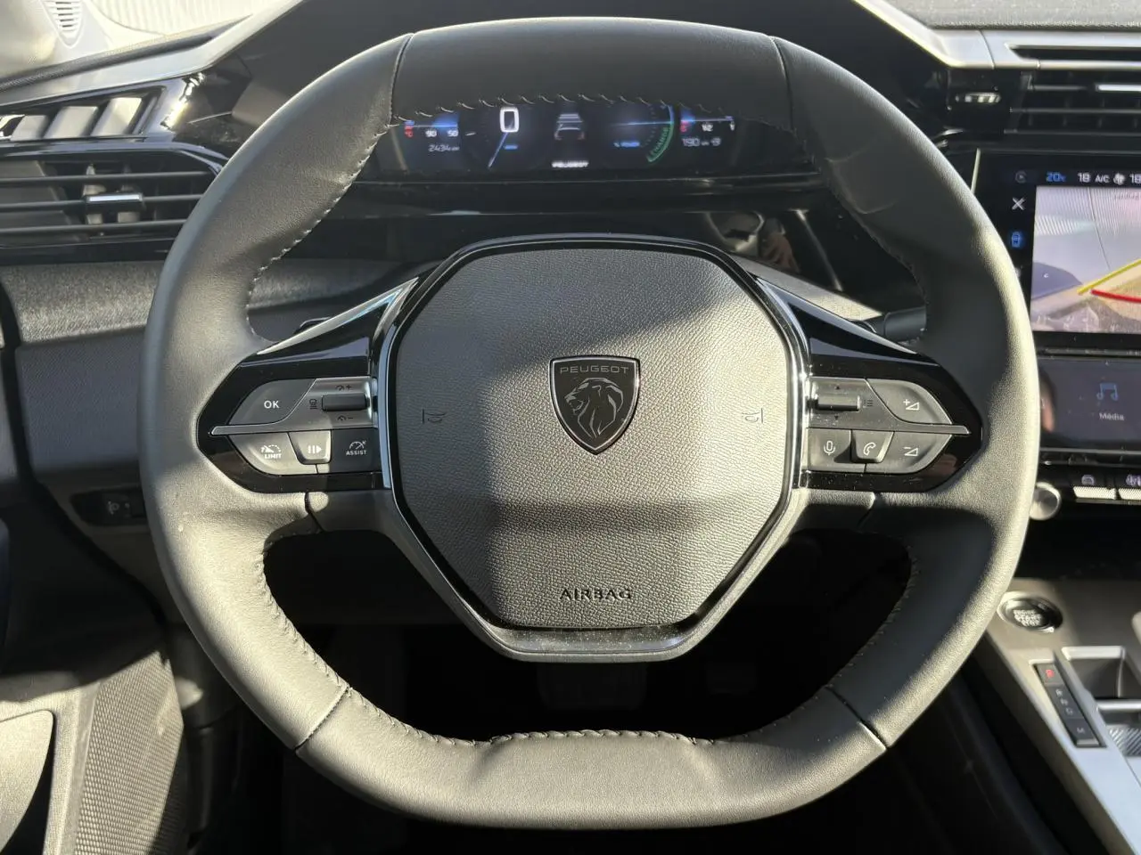 Vue rapprochée du volant cuir noir de la Peugeot 308 Hybrid 2025 avec tableau de bord numérique et écran tactile.
