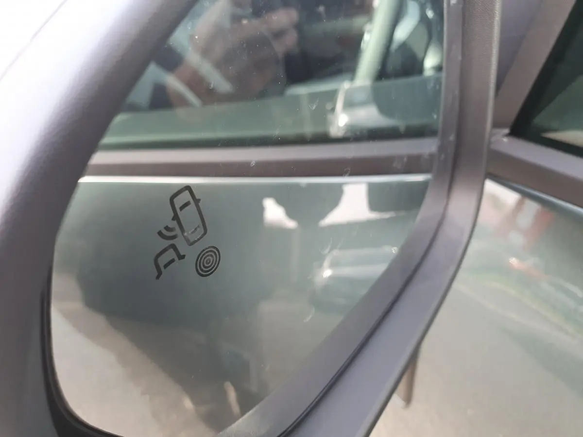 Gros plan sur le rétroviseur droit vert cèdre du Dacia Bigster 2026 avec icône d'alerte d'angle mort visible.