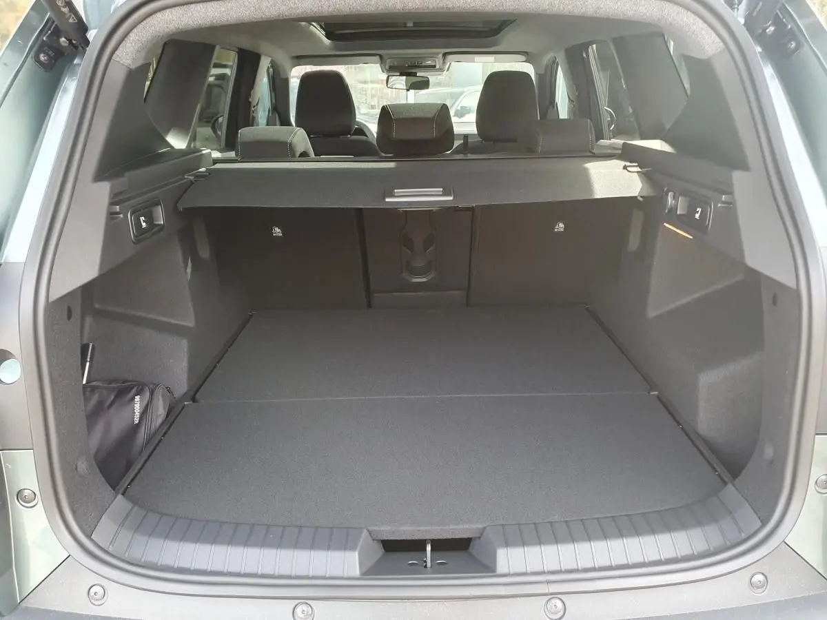 Coffre ouvert vu de l'arrière du Dacia Bigster vert cèdre, avec banquette arrière rabattue et cache-bagages en place.