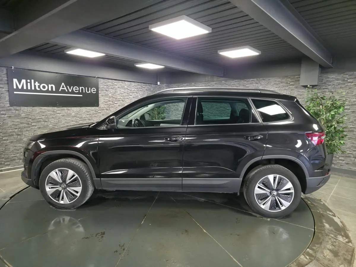 Vue de profil côté gauche d’un Skoda Karoq noir 2023 en intérieur, avec jantes alliage et vitres surteintées.