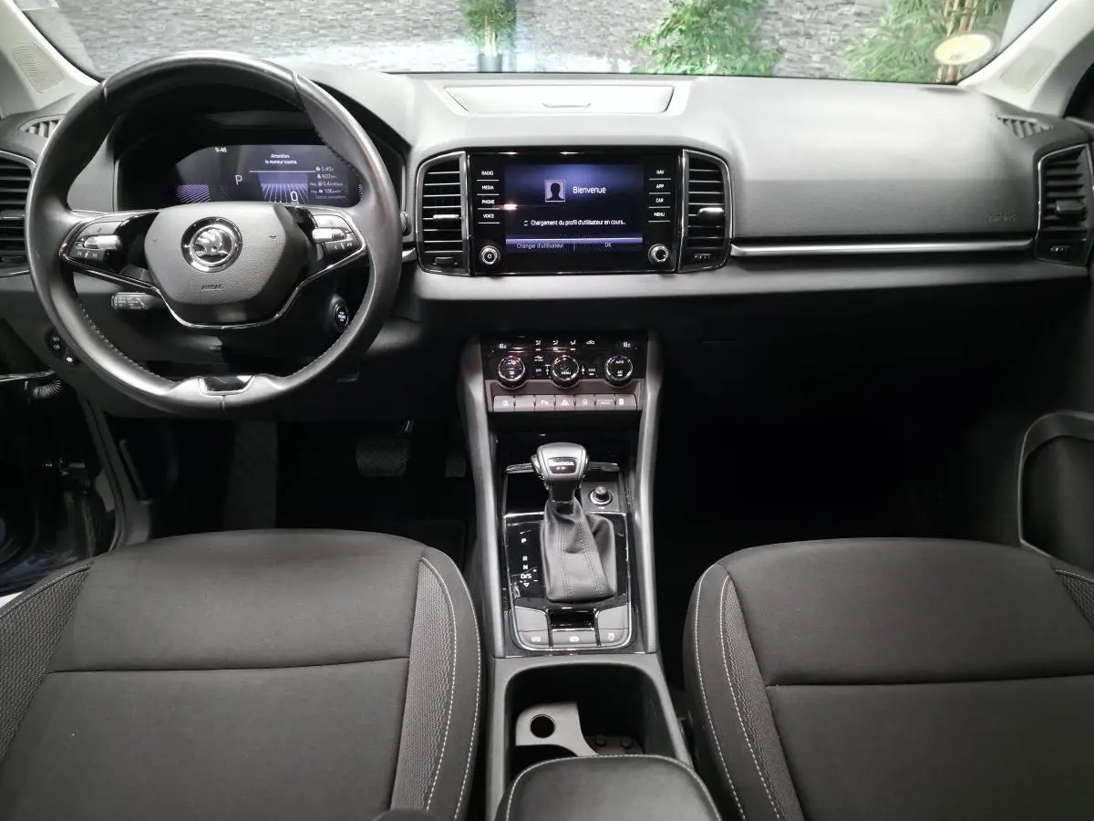 Vue intérieure frontale du tableau de bord et console centrale noire du Skoda Karoq 2023 avec volant cuir et écran tactile.