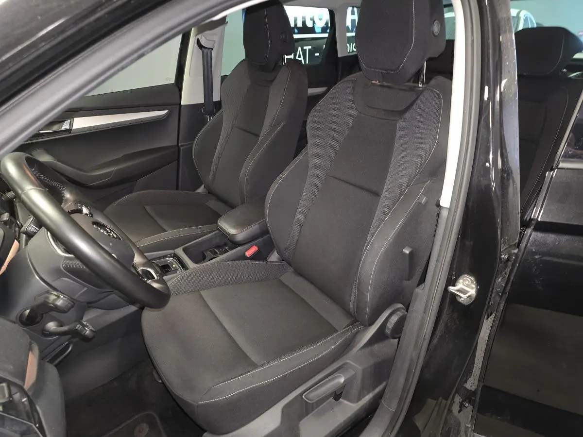 Vue intérieure côté conducteur du Skoda Karoq noir 2023, sièges tissu Ambition noirs avec accoudoir central.