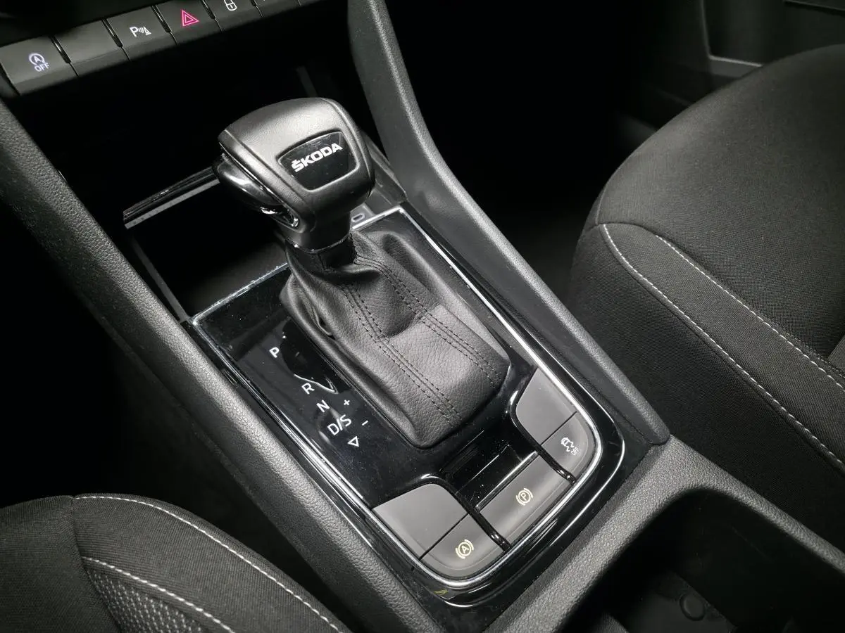 Gros plan sur le levier de vitesse automatique noir ŠKODA KAROQ 2023 avec coutures apparentes et commandes autour.