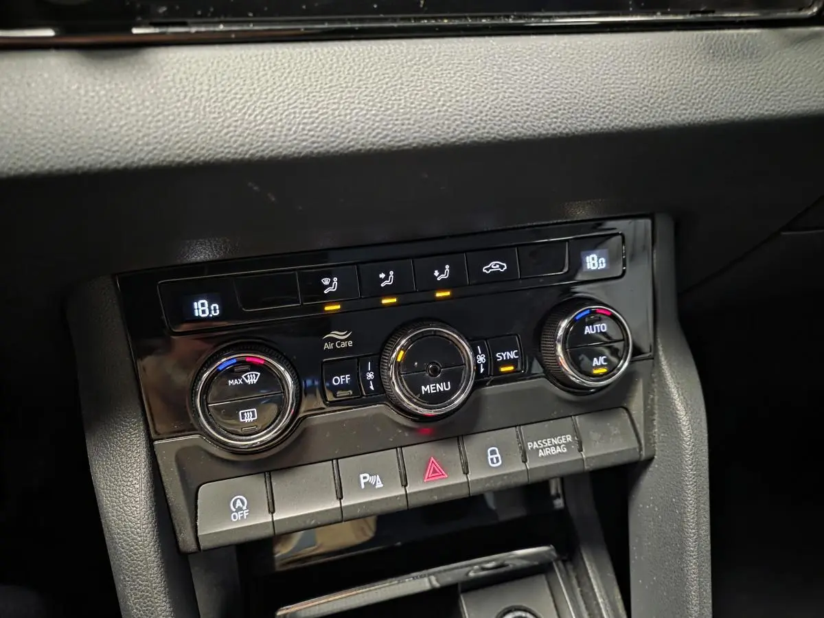 Gros plan sur la console centrale noire du Skoda Karoq 2023, avec commandes de climatisation automatique bi-zone et boutons fonctionnels.