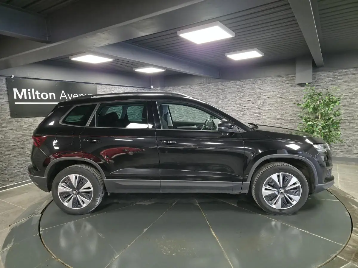 Vue de profil côté gauche d'un Skoda Karoq noir 2023 avec jantes alliage et barres de toit en intérieur showroom.