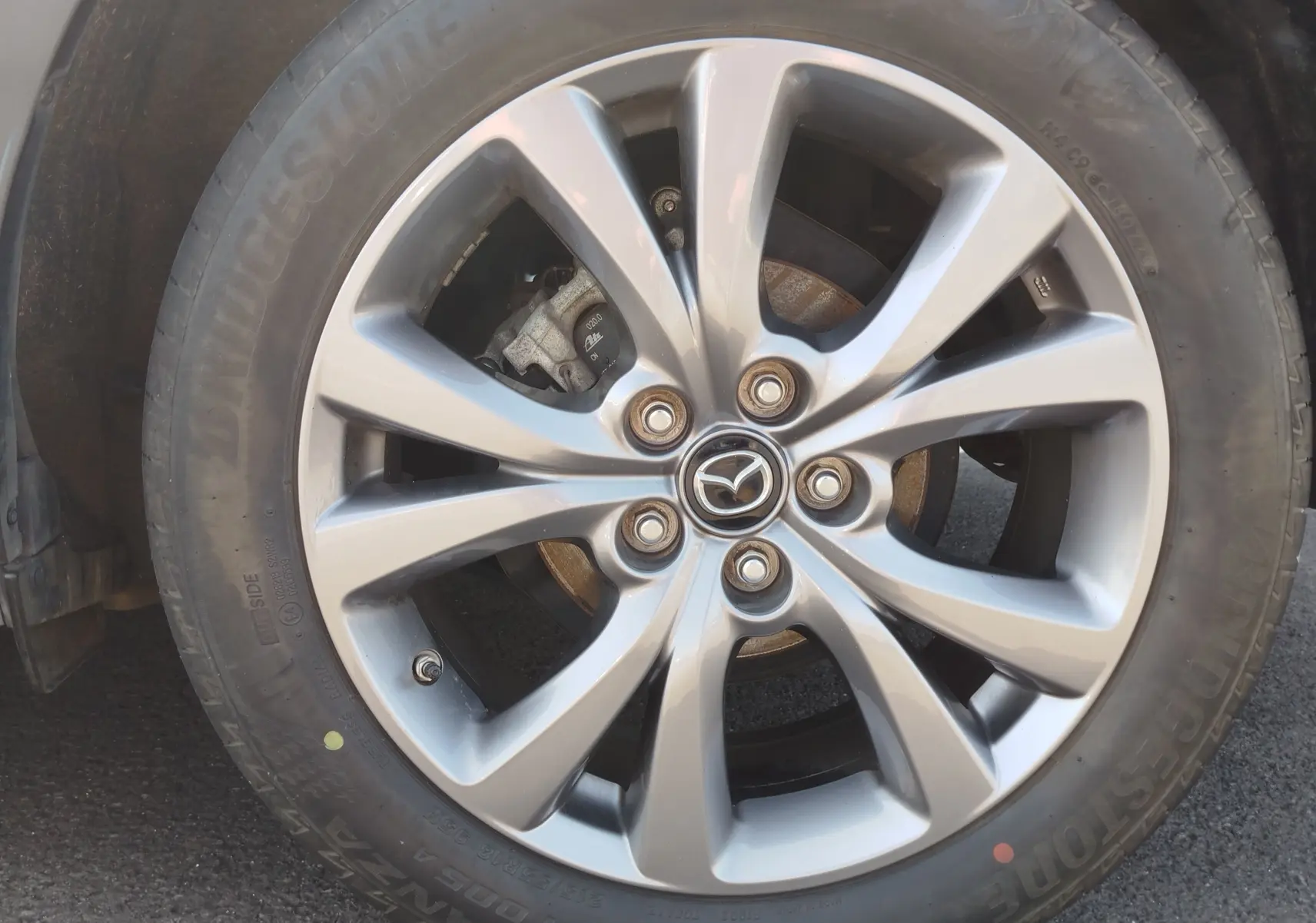Gros plan sur la jante alliage argentée avec logo Mazda au centre, montée sur un pneu Bridgestone noir.