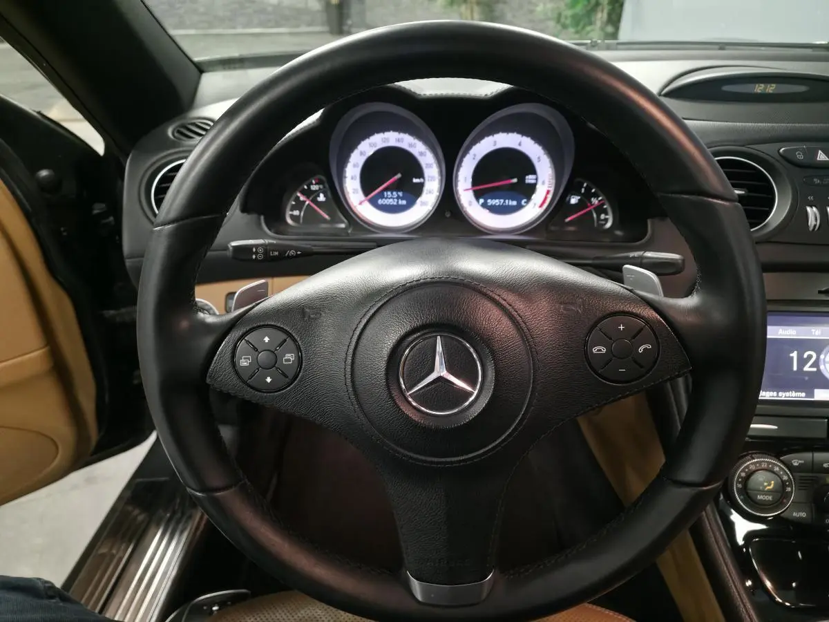 Vue rapprochée du volant cuir noir multifonctions d'une Mercedes SL 500 de 2008 avec tableau de bord éclairé.