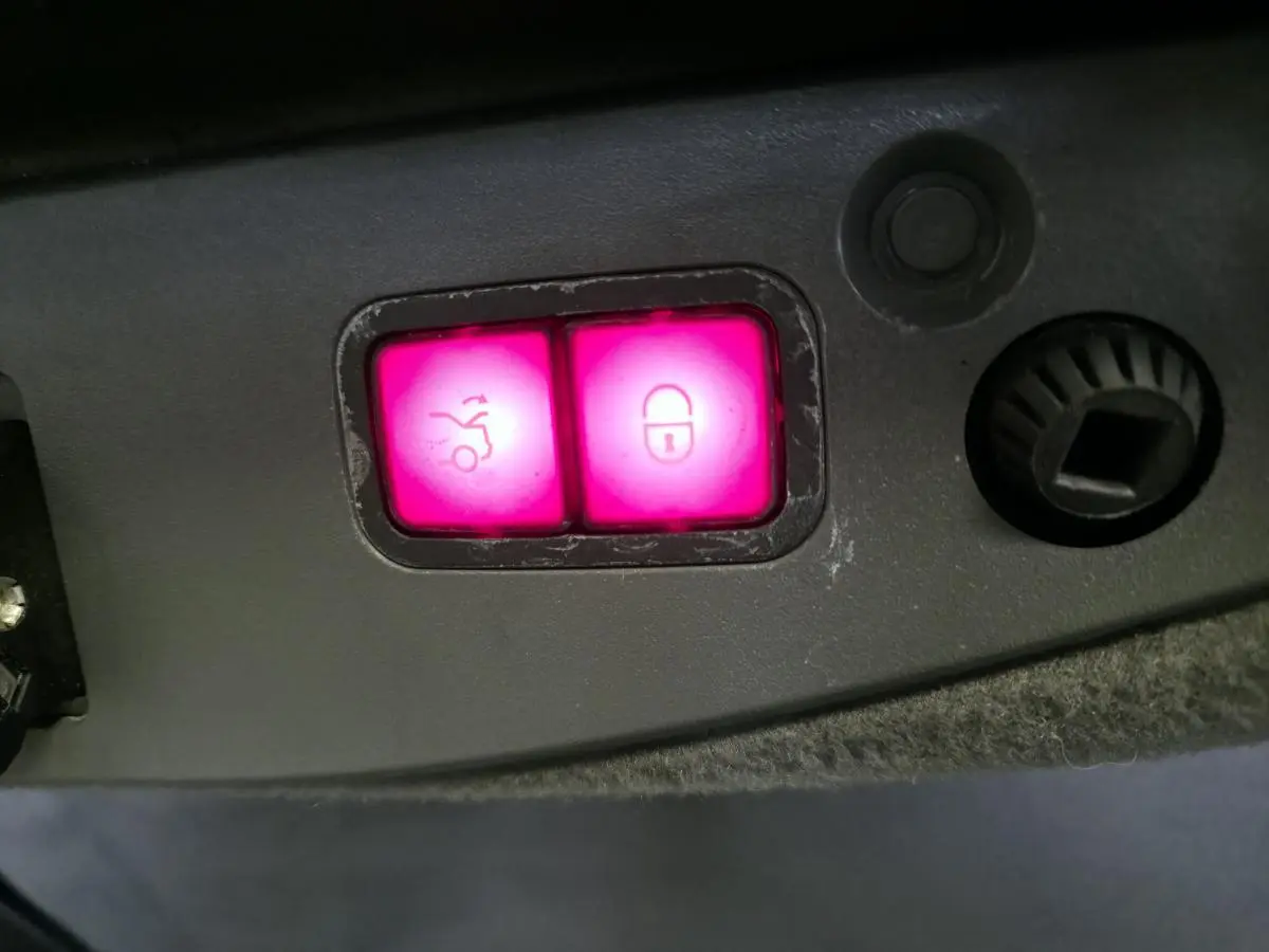 Gros plan sur les boutons lumineux roses de fermeture électrique du coffre et de verrouillage dans le coffre d'une Mercedes SL 500 noire.