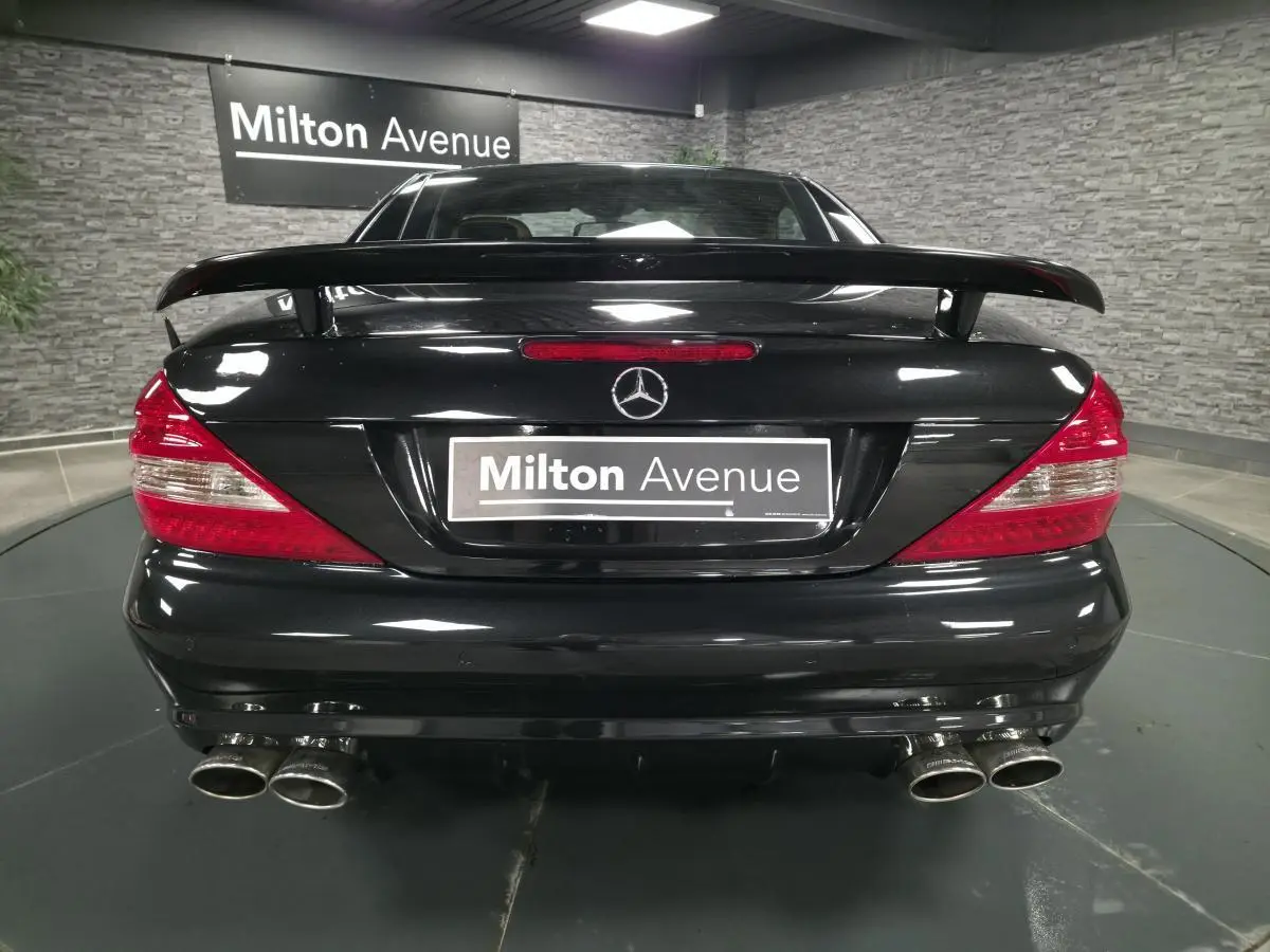 Vue arrière d'une Mercedes SL 500 noire avec aileron et quadruple sortie d'échappement dans un showroom.