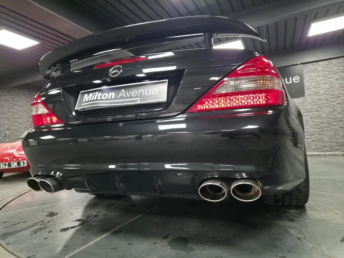 Vue arrière basse d'une Mercedes SL 500 noire avec double sortie d'échappement et aileron AMG en intérieur showroom.