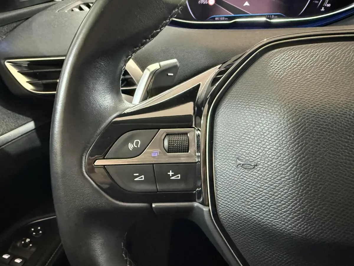 Gros plan sur le côté gauche du volant cuir noir du Peugeot 5008 2021 avec commandes multifonctions et palettes au volant.