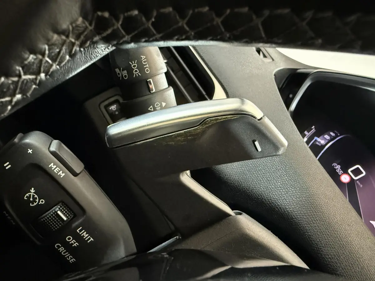 Gros plan sur le levier de commande et le volant en cuir noir du Peugeot 5008 gris clair, tableau de bord numérique partiellement visible.