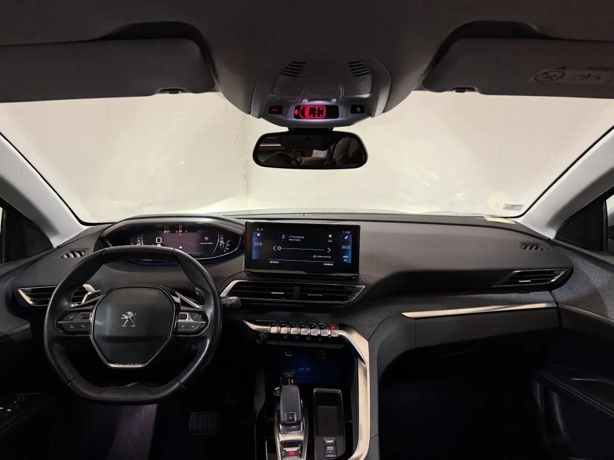Vue intérieure avant du Peugeot 5008 gris clair, tableau de bord moderne avec écran tactile central et volant cuir multifonctions.