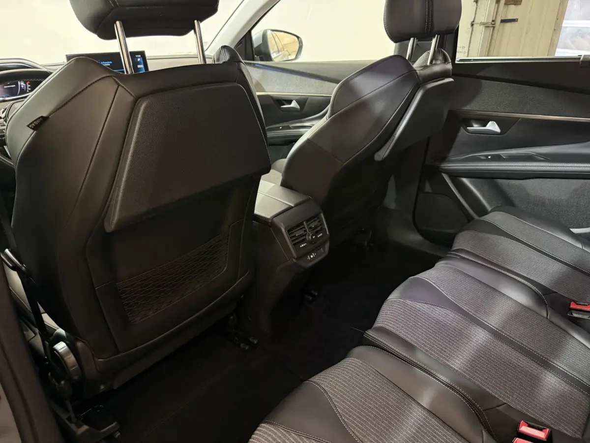 Vue intérieure arrière droite du Peugeot 5008 gris clair, sièges en cuir noir et console centrale avec aérateurs et ports USB.
