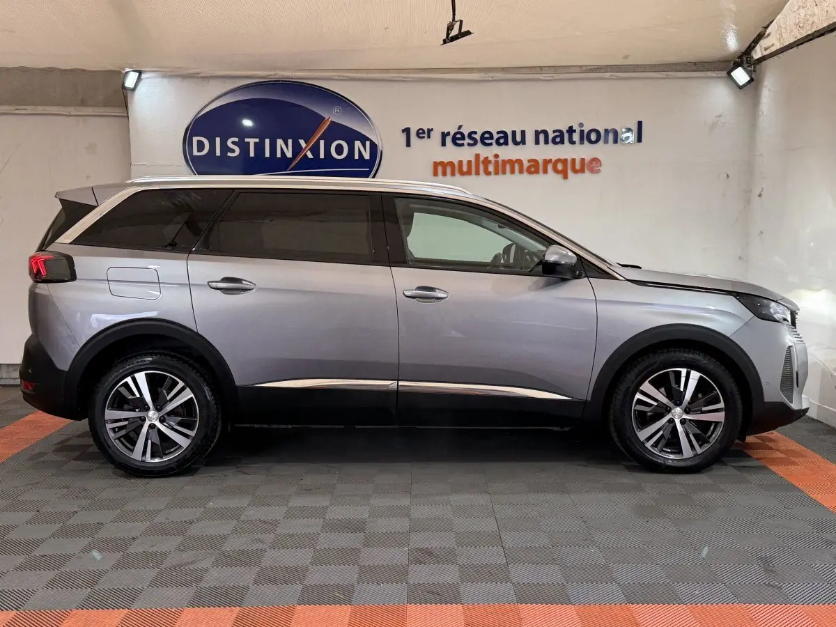 Vue latérale droite d’un Peugeot 5008 gris clair 2021 avec jantes alliage et vitres teintées en intérieur showroom.