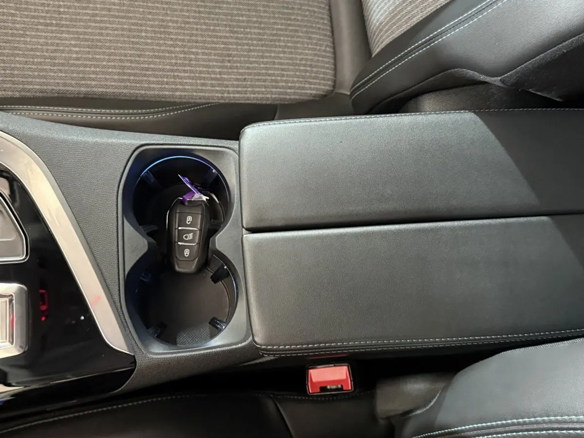 Vue rapprochée de la console centrale noire avec porte-gobelets et clé de voiture dans un Peugeot 5008 gris clair.