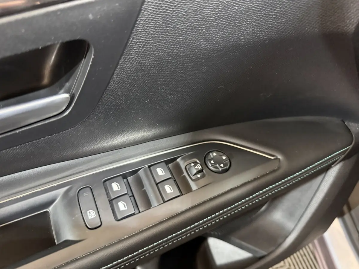 Gros plan sur la commande des vitres électriques côté conducteur du Peugeot 5008 gris clair, avec surpiqûres bleues.