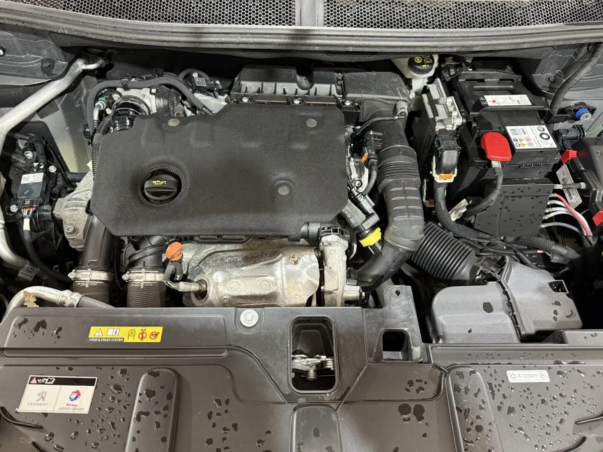 Vue rapprochée du moteur diesel Peugeot 5008 2021, avec capot ouvert et composants visibles sous la pluie.