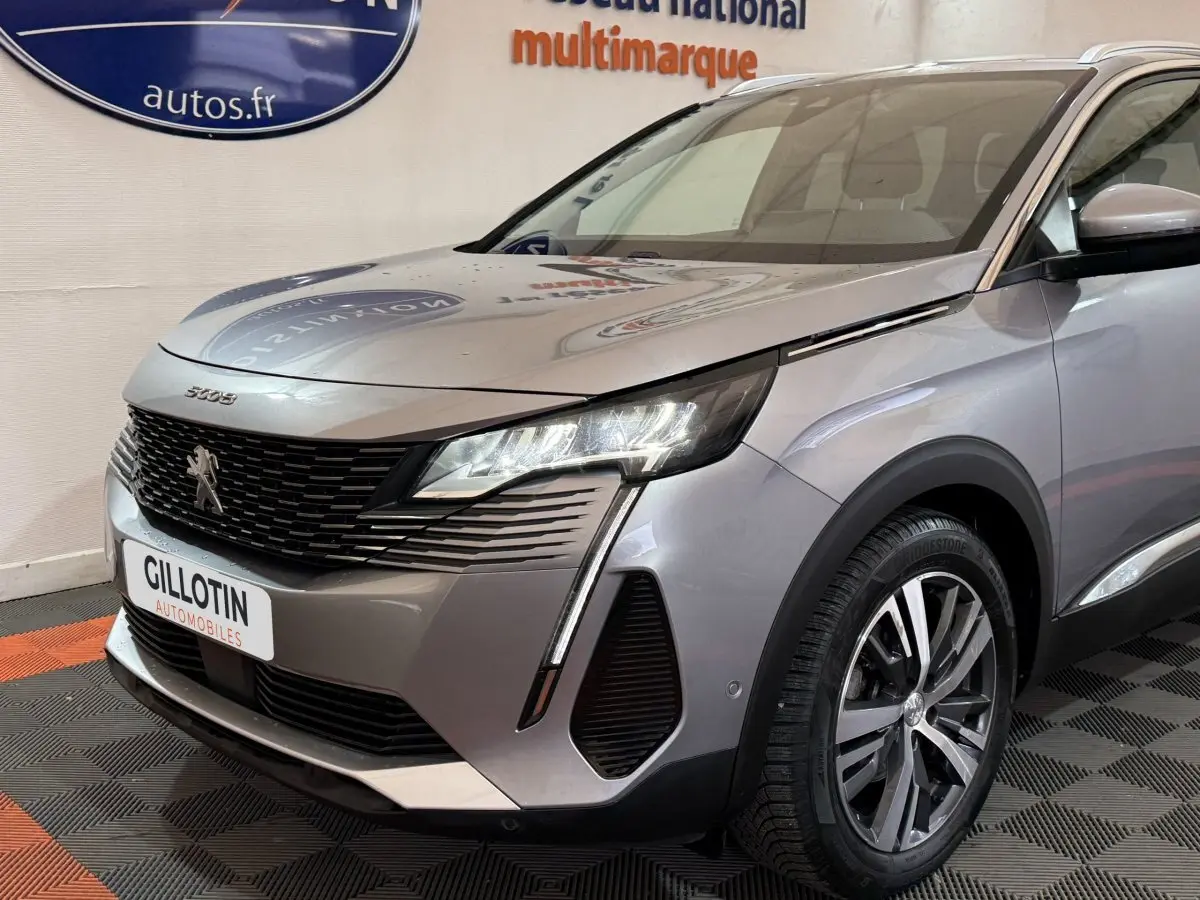 Vue 3/4 avant droit d’un Peugeot 5008 gris clair avec phares LED et calandre noire texturée.