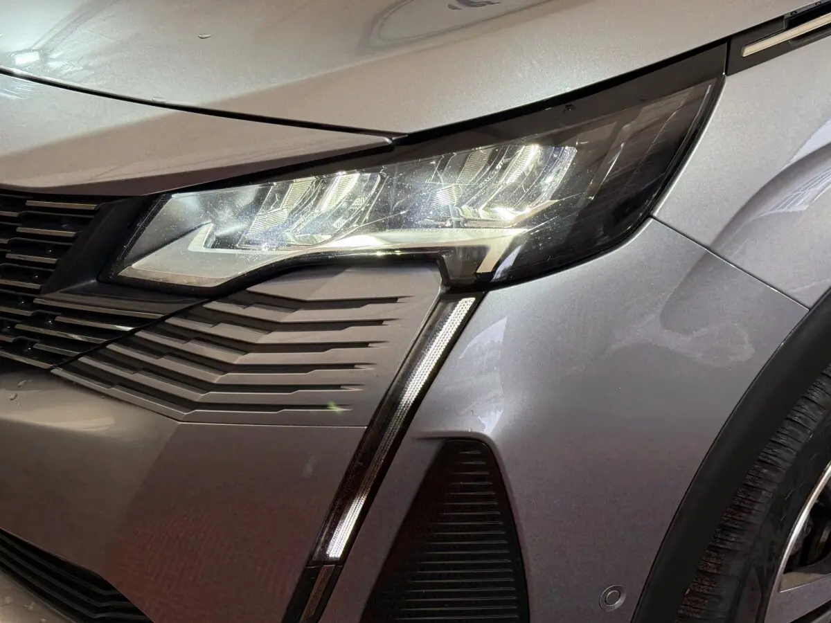 Gros plan sur le phare avant droit du Peugeot 5008 gris clair, mettant en valeur la signature lumineuse LED verticale.