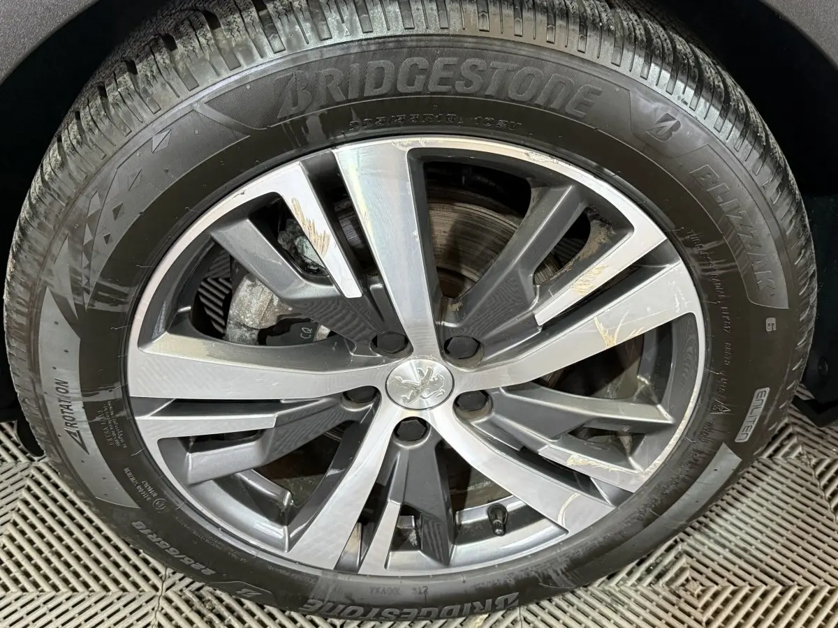 Gros plan sur la jante alliage gris et argentée avec logo Peugeot, montée sur pneu Bridgestone Blizzak.