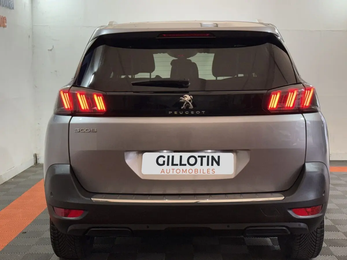 Vue arrière d’un Peugeot 5008 gris clair 2021 avec feux arrière LED allumés et logo central visible.