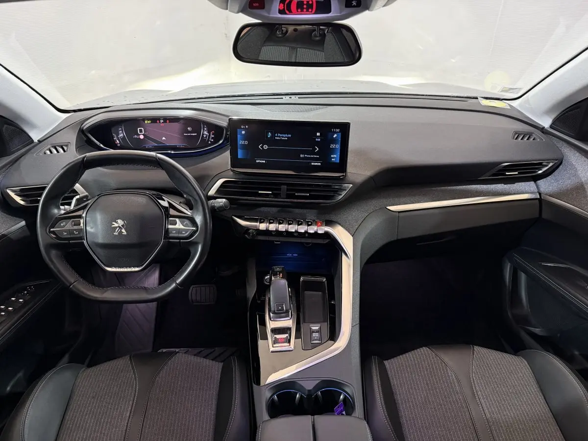 Vue intérieure avant du Peugeot 5008 gris clair, tableau de bord moderne avec écran tactile central et volant compact cuir.