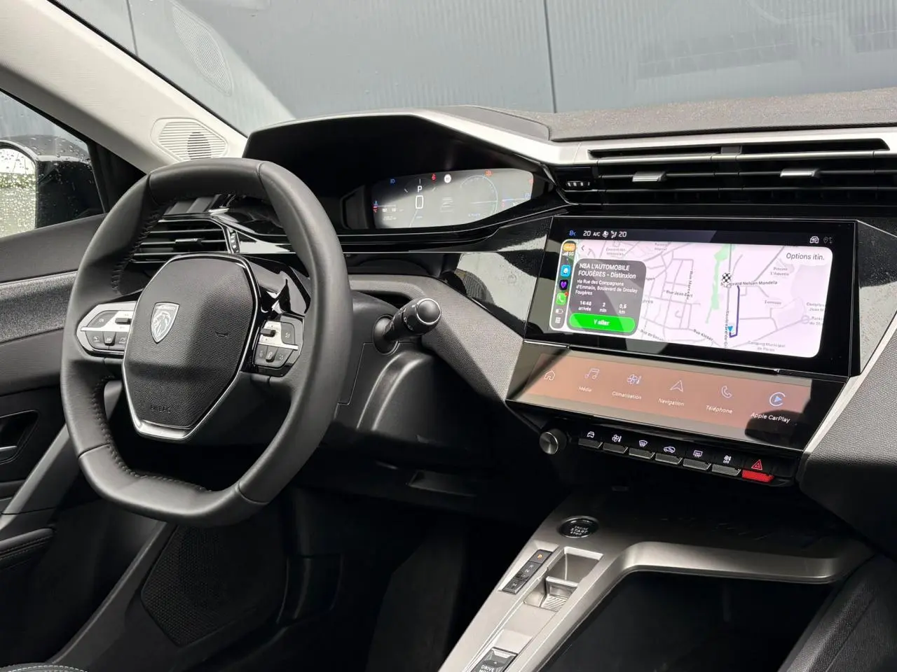 Vue intérieure du poste de conduite de la Peugeot 308 SW Hybrid 2025, avec écran tactile affichant la navigation et volant cuir noir.