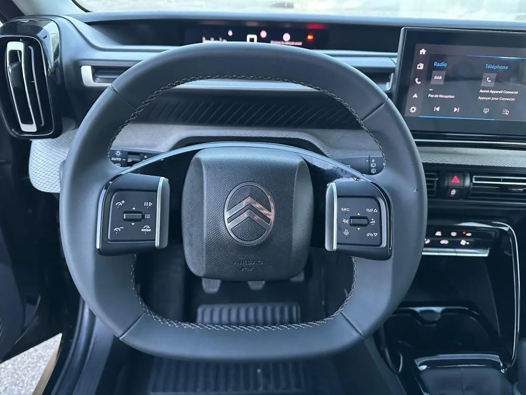 Vue intérieure centrée sur le volant noir de la Citroën C3 2025 avec commandes intégrées et écran tactile visible.