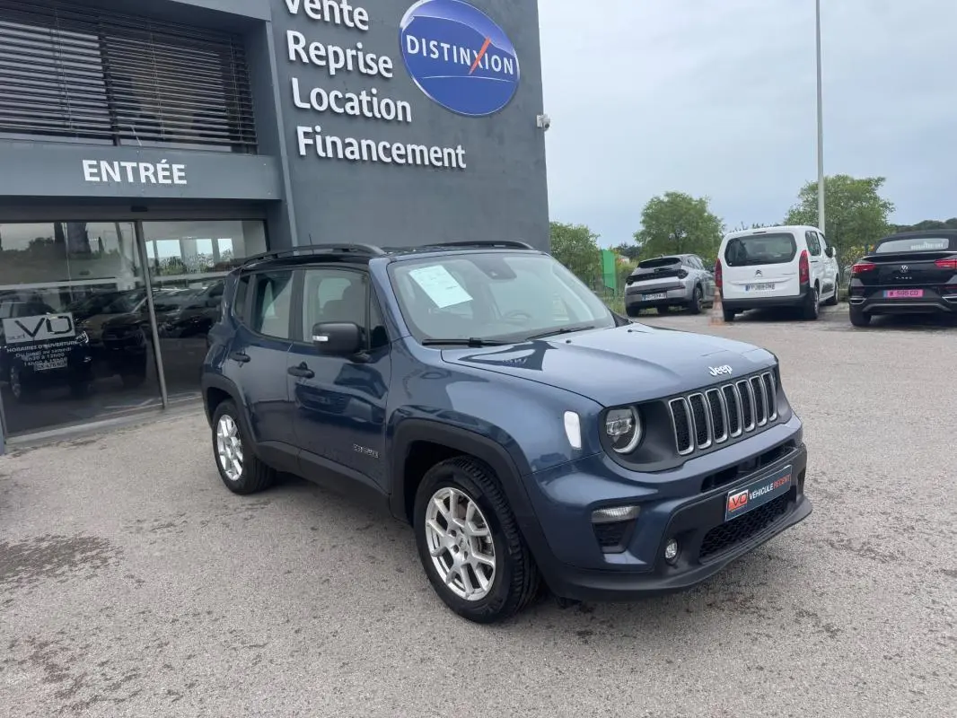 Jeep Renegade bleu en 3/4 avant droit, avec barres de toit et jantes alliage 17 pouces, stationné devant un concessionnaire.