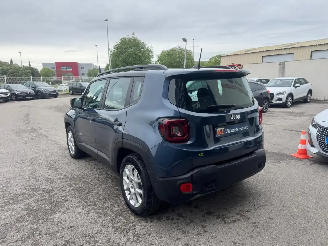 Jeep Renegade bleu en 3/4 arrière droit, avec barres de toit et jantes alliage 17 pouces visibles.