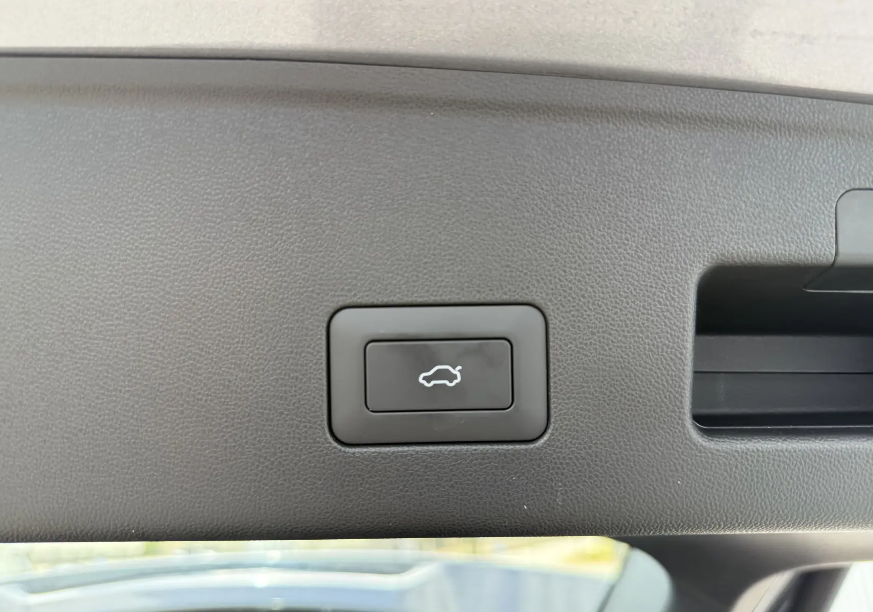 Bouton d'ouverture électrique du coffre sur la garniture intérieure noire du hayon d'un JAECOO J5 Phantom Grey 2026.