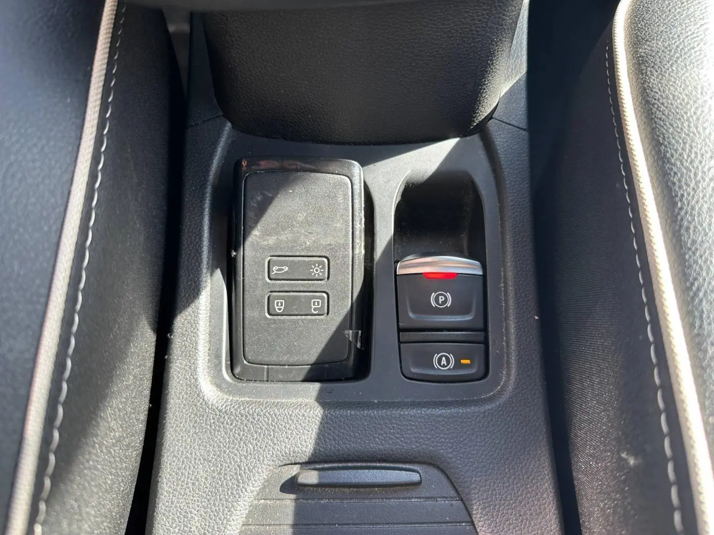 Gros plan sur la console centrale noire de la Renault Clio 1.0 Eco-G 100ch Techno avec commandes électroniques et accoudoir.