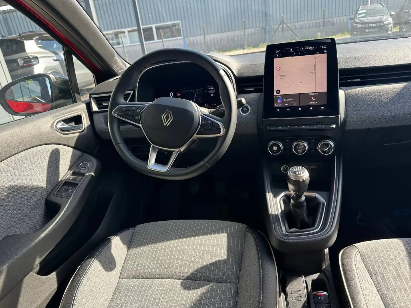 Vue intérieure côté conducteur de la Renault Clio 2025, volant multifonction et écran tactile central visibles.