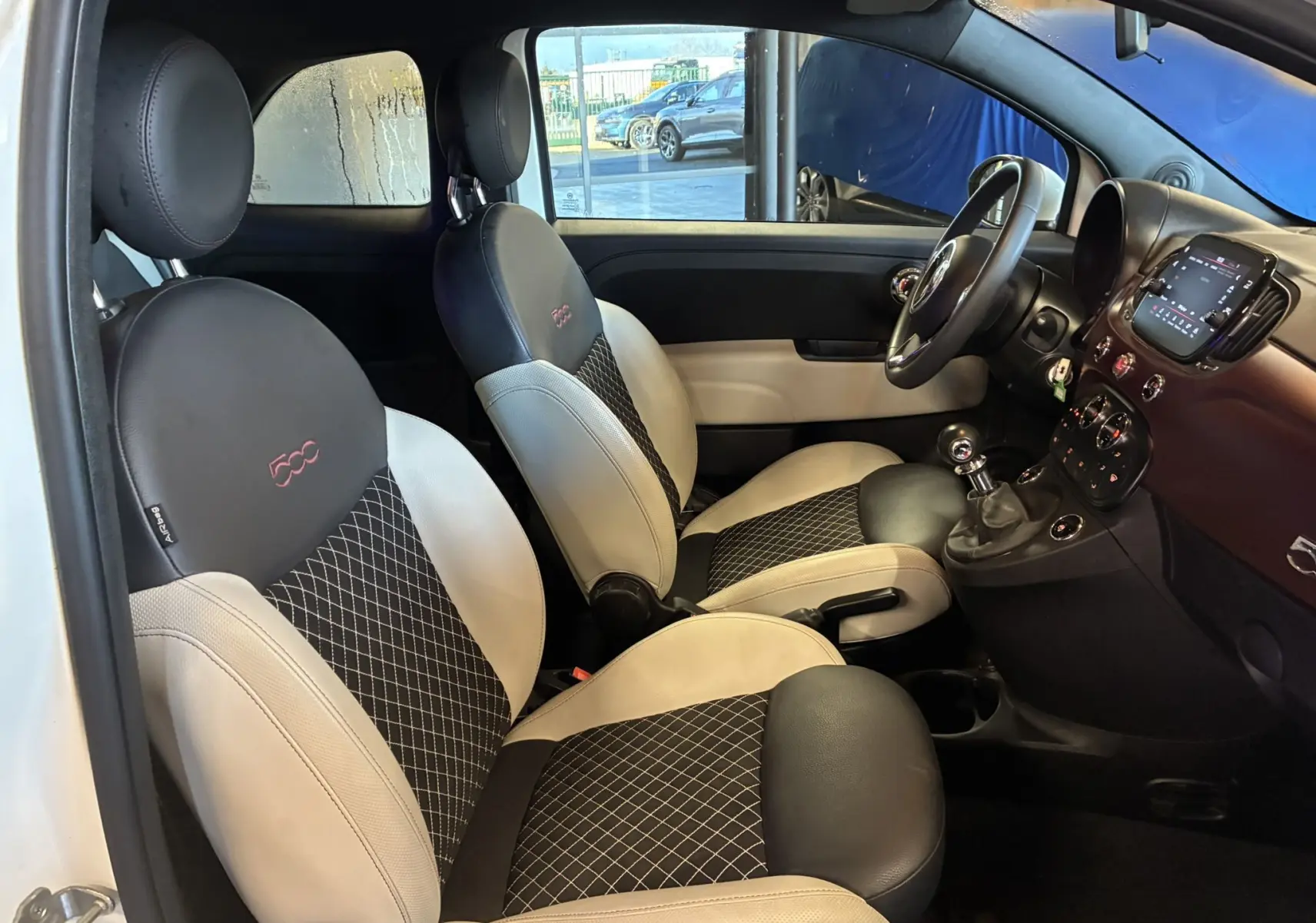 Vue intérieure côté gauche de la Fiat 500 blanche, mettant en valeur les sièges bicolores noirs et beige avec logo 500 brodé.