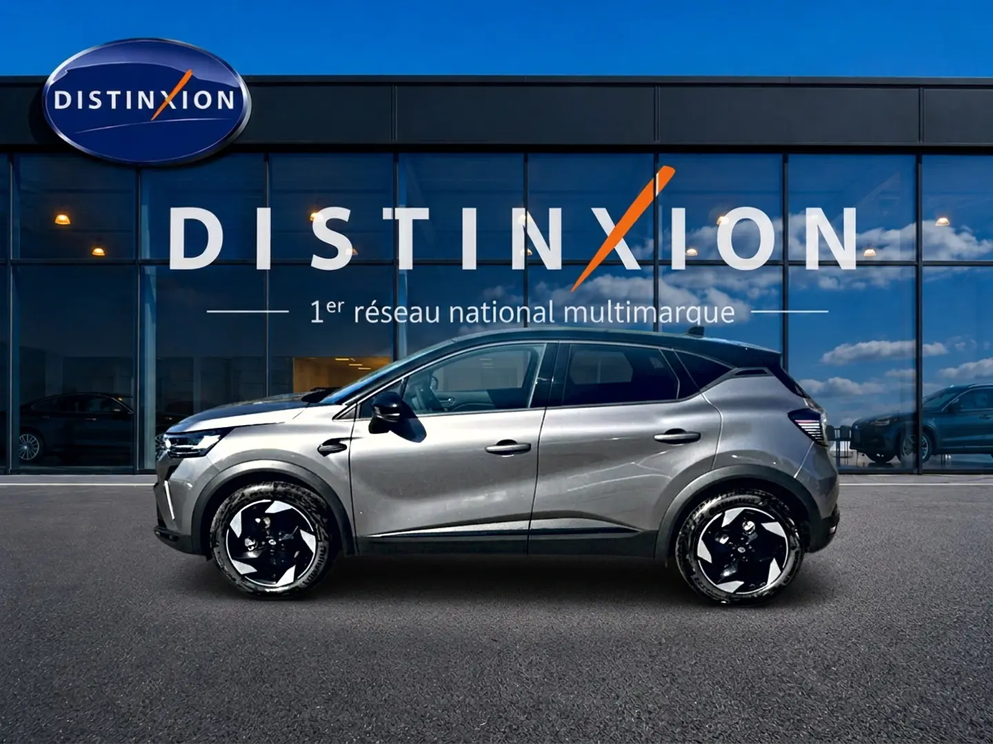 Profil droit d'un Renault Captur gris cassiopée 2026, avec jantes alu noires et toit noir, devant une vitrine Distinxion.