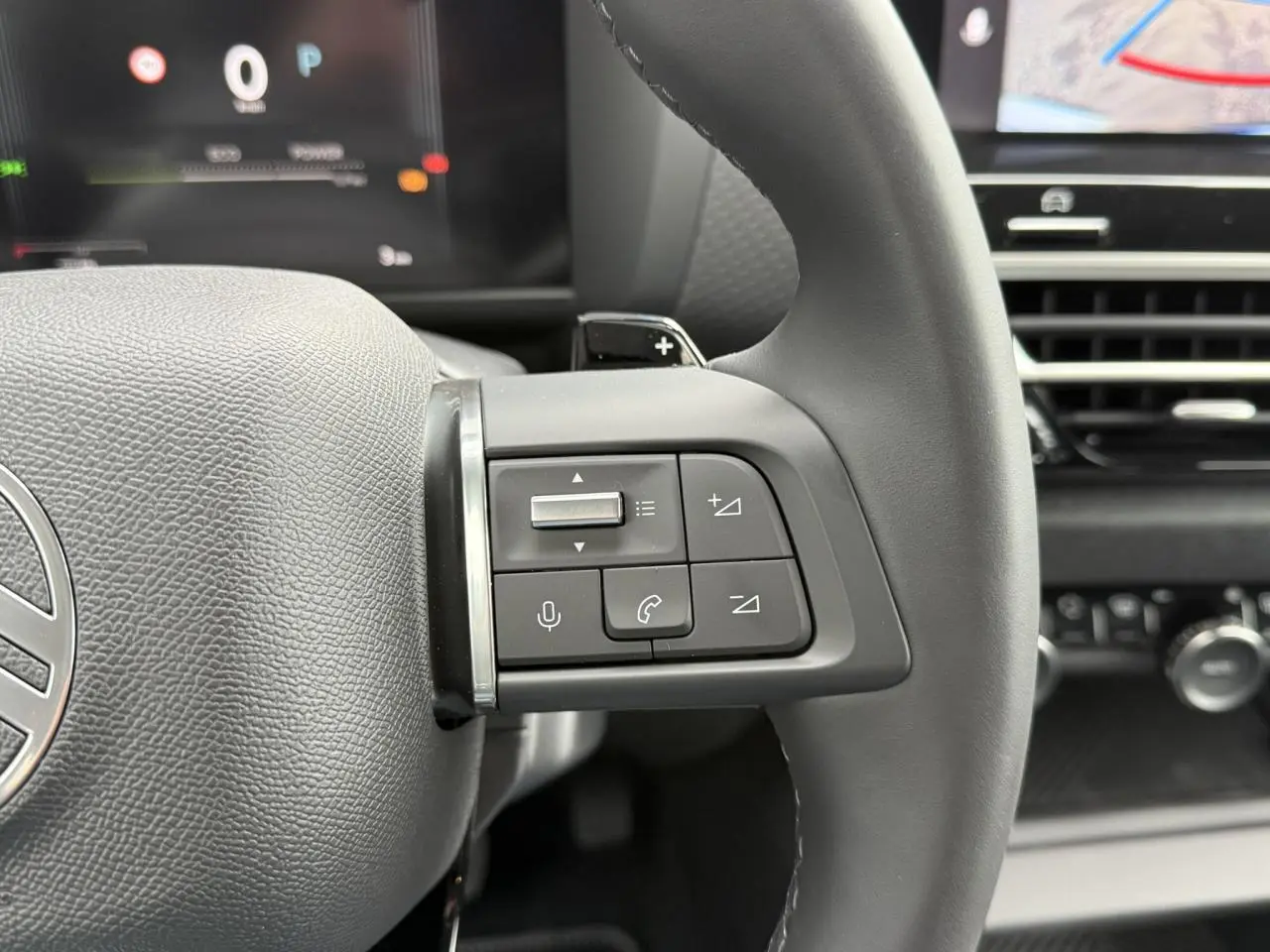 Gros plan sur les commandes au volant gauche du Citroën C4 blanc, avec affichage numérique en arrière-plan.