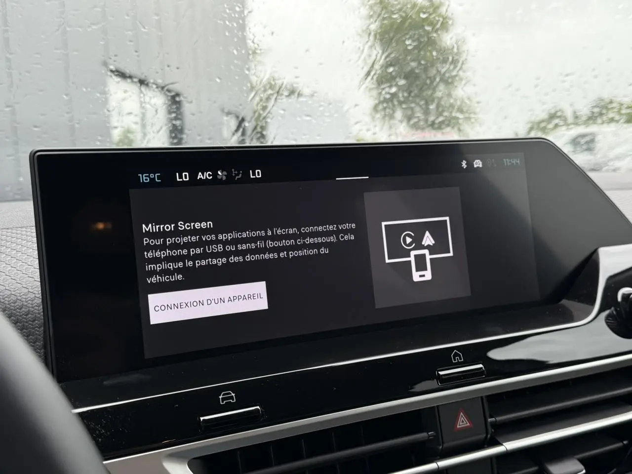 Écran tactile central de la Citroën C4 hybride 2025 affichant la fonction Mirror Screen sous pluie extérieure.