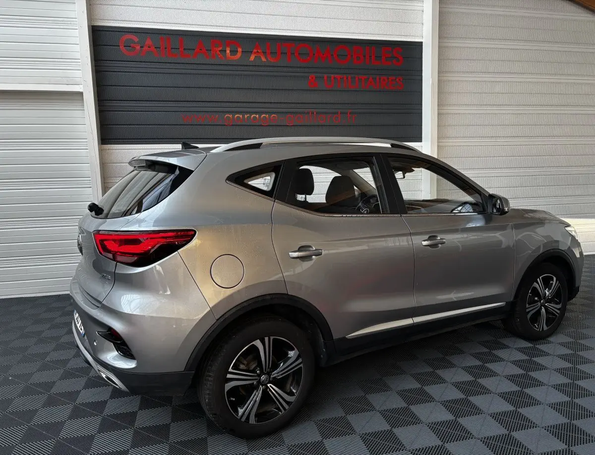 Vue 3/4 arrière côté droit d’un SUV MG ZS gris clair 2022 avec jantes alliage et feux arrière LED allumés.
